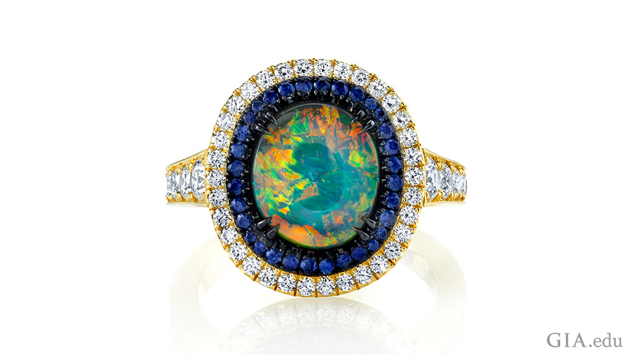 Sapphires and diamonds encircle a 1.92 carat (ct) black opal in this stunning 18K yellow gold and black rhodium ring. Courtesy: Omi Privé