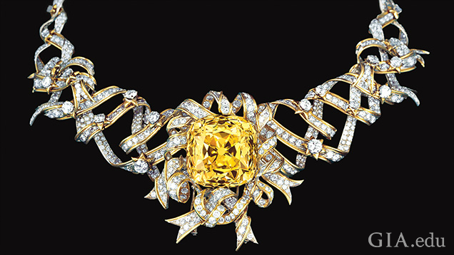 A large rosette cut yellow diamond is framed and sits on a ribbons of diamonds. A large rosette cut yellow diamond is framed and sits on a ribbons of diamonds.