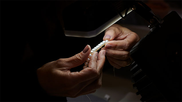 Close-up of hands holding a strand of pearl under a light source. 