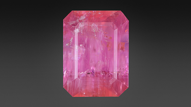 Figure 1. This 8.13 ct pezzottaite contains delicate growth banding (~horizontal) and tube inclusions (~vertical, seen best in lower left). Photo by Adriana Robinson. Figure 1. This 8.13 ct pezzottaite contains delicate growth banding (~horizontal) and tube inclusions (~vertical, seen best in lower left). Photo by Adriana Robinson.