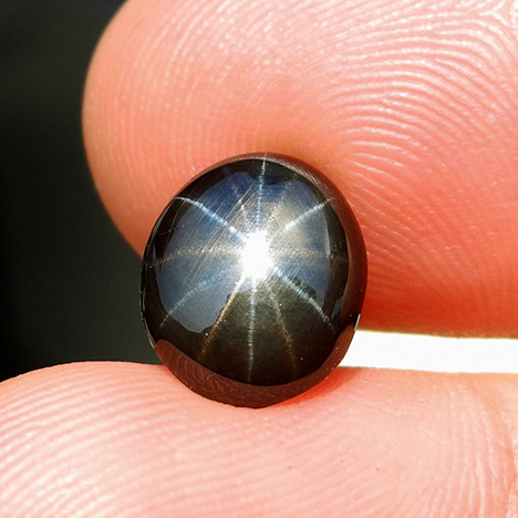 A black star sapphire with one set of golden rays and another set of silver rays. A black star sapphire with one set of golden rays and another set of silver rays.