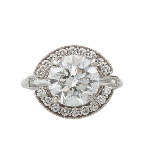 Top view of a platinum solitaire ring containing a round brilliant center diamond and baguette side diamonds. A white gold halo set with small round