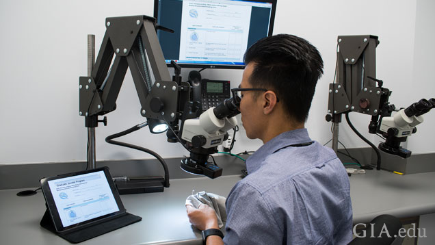 Man sits in front of a microscope to examine a piece of jewelry.