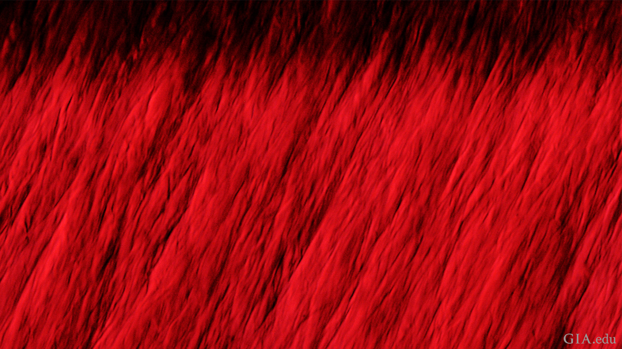 Chevron-shaped graining is diagnostic of the hydrothermal growth method used to produce this Tairus synthetic ruby. Field of view 1.22 mm. Photomicrograph by GIA staff.