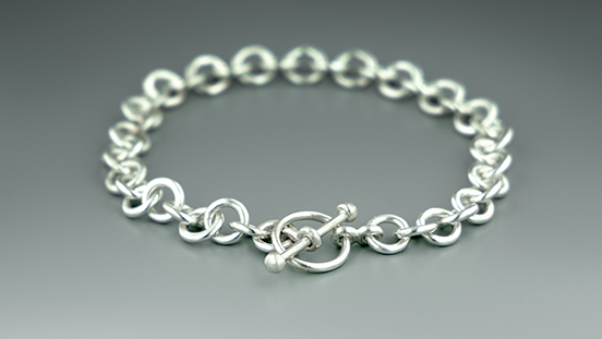 Create a handmade chain and toggle clasp in sterling silver. Learn skills like soldering, chain assembly, forming a wire loop, fusing metal with a torch, and making a toggle clasp