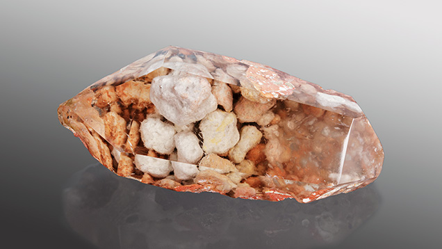 Figure 1. This 150.97 ct quartz crystal hosts pebbles of an amphibole, stacked like rocks in a stone wall. Photo by Annie Haynes. Figure 1. This 150.97 ct quartz crystal hosts pebbles of an amphibole, stacked like rocks in a stone wall. Photo by Annie Haynes.