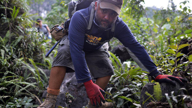 Diaz needs to crouch low as he makes his way through jungle terrain with a backpack on. He wears boots and gloves to protect him on the uncut path. Diaz needs to crouch low as he makes his way through jungle terrain with a backpack on. He wears boots and gloves to protect him on the uncut path.