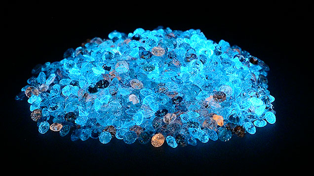 A pile of loose, laboratory-grown diamonds glowing blue under UV light due to their phosphorescence A pile of loose, laboratory-grown diamonds glowing blue under UV light due to their phosphorescence