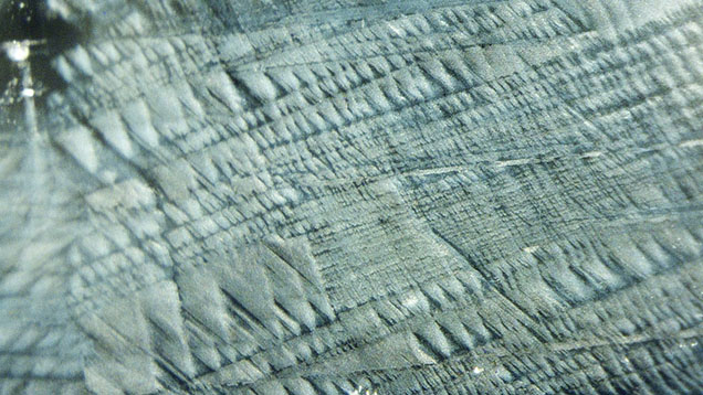 Clouds of particles in sapphire resembling tire marks in snow. Photomicrograph by Shunsuke Nagai, field of view 2.30 mm.