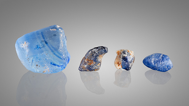 Submitted set contains manmade glass (left), two laboratory-grown sapphires with imitation matrix (center), and natural blue sapphire rough (right).