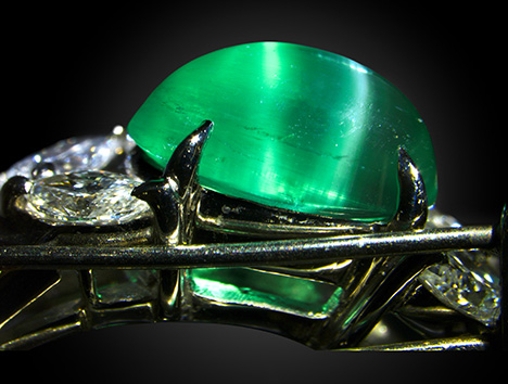 Figure 2. Side view of the emerald ring. Parallel tube inclusions are oblique to the pavilion. The white reflection on the right is caused by the inclusions near the surface of the curved cabochon, while the greenish reflection on the left is caused by the reflection off of the bottom face of the cabochon. Photo by Shunsuke Nagai.