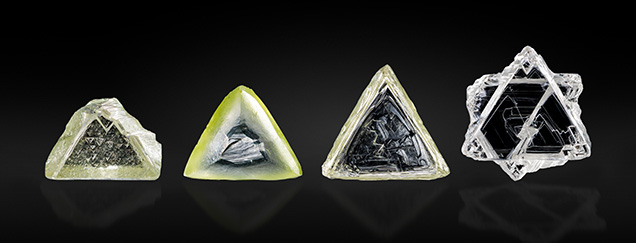 Figure 1. Examples of contact-twinned macle diamond crystals from South Africa. Left to right: a flat triangular macle with limited resorption (sample 11; 0.357 ct); an extensively resorbed variant of a flat triangular macle (sample 12; 0.411 ct); a very elongated flat macle with stacking growth layers on the octahedral faces, showcasing sharp edges and pointed apex corners (sample 13; 0.553 ct); a six-pointed star-shaped, poorly resorbed flat macle (sample 14; 0.747 ct). Photo by Tetsuya Chikayama; courtesy of Suwa & Son, Inc.