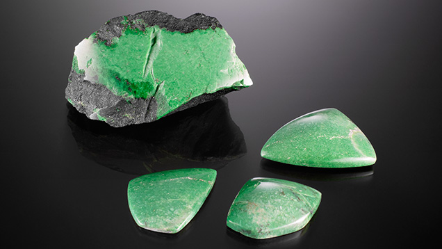 This 110.4 g partially polished rough grossular garnet “Transvaal jade” and three polished cabochons (41.95–92.87 ct) display unusually vibrant green colors between seams of dark chromite matrix. Photo by Diego Sanchez; courtesy of TMS Gems.