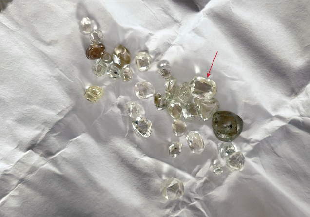 Figure 3. A parcel of rough diamonds, collected over a month by a Liberian artisanal miner. The diamond indicated by the arrow weighs 0.80 ct. Photo by Beth West.