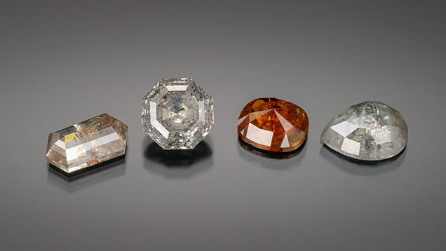 Figure 2. “Salt and pepper” diamonds. Left to right: a 4.30 ct hexagonal step cut, a 5.56 ct octagonal step cut, a 3.58 natural-color orange cushion cut, and a 3.39 ct pear cut. Photo by Robert Weldon; courtesy of Misfit Diamonds.