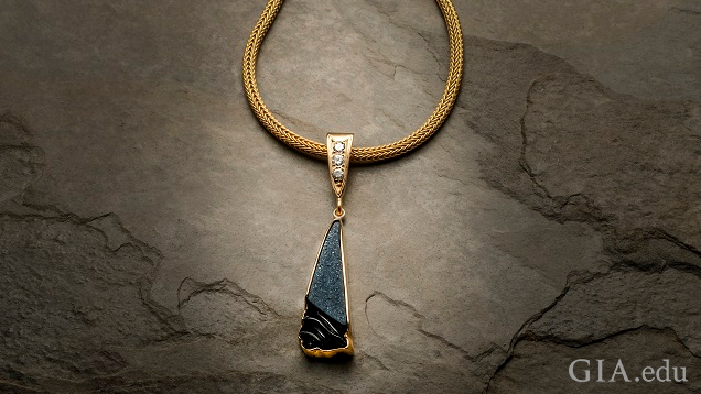 一件三角形的黑色条纹玛瑙晶簇雕刻品,周围镶嵌着一圈 14k 黄金。它挂在黄金链的一个三角形黄金夹件上,并镶有三颗 0.10 分的钻石。 一件三角形的黑色条纹玛瑙晶簇雕刻品,周围镶嵌着一圈 14k 黄金。它挂在黄金链的一个三角形黄金夹件上,并镶有三颗 0.10 分的钻石。