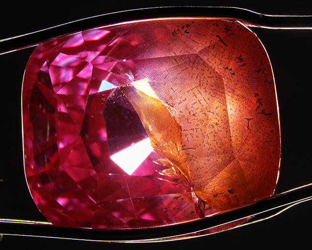 Pink-orange synthetic sapphire contains large fractures with orange staining.