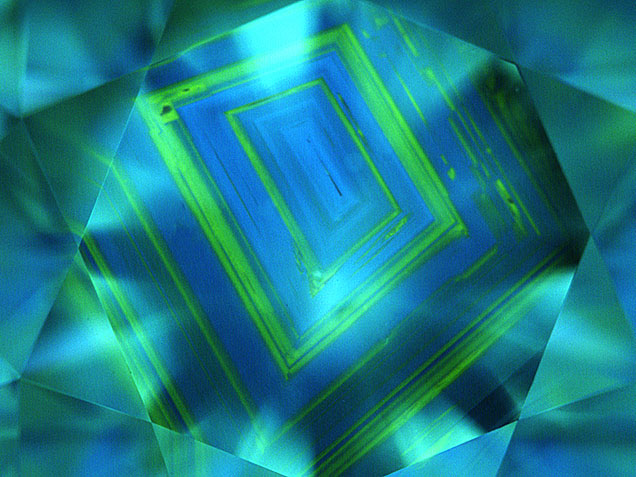 Figure 14. Natural type Ia diamonds often show a growth pattern that has been compared to the growth rings of a tree. However, it is not as common to see the alternating pattern of blue fluorescence (due to the N3 center) and green (due to H3/H4 centers) shown in this 1.83 ct K-color diamond with SI2 clarity. PL spectroscopy is very useful for confirming these centers and for detecting much weaker optical centers. Image by GIA staff. Figure 14. Natural type Ia diamonds often show a growth pattern that has been compared to the growth rings of a tree. However, it is not as common to see the alternating pattern of blue fluorescence (due to the N3 center) and green (due to H3/H4 centers) shown in this 1.83 ct K-color diamond with SI2 clarity. PL spectroscopy is very useful for confirming these centers and for detecting much weaker optical centers. Image by GIA staff.